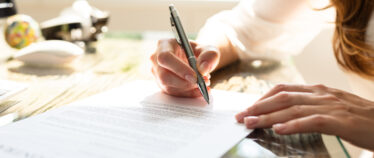 close-up image of businesswoman's hand holding a writing pen and preparing to write on or sign a document.